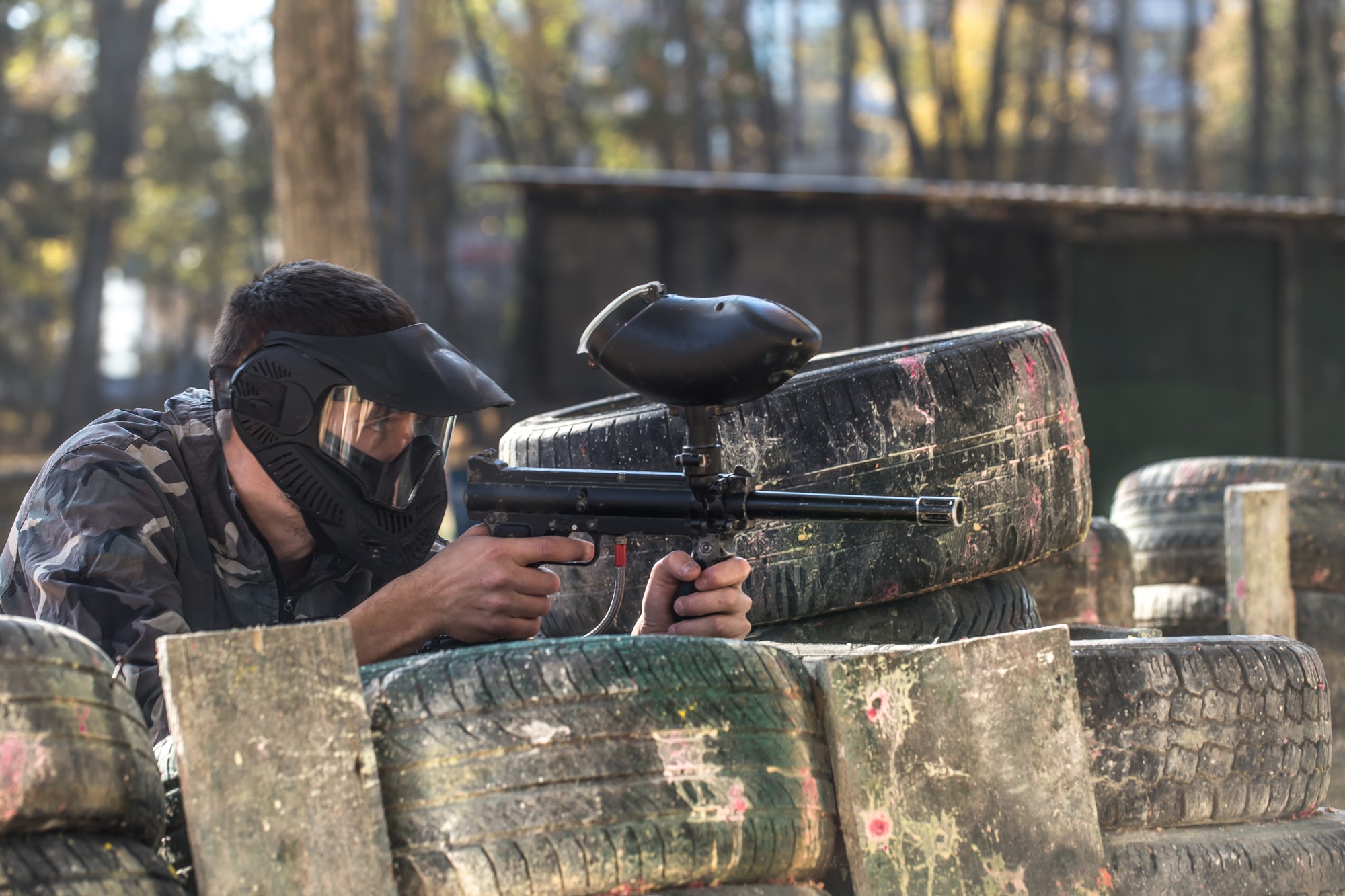 Joueur de paintball visant depuis un abri de pneus sur un terrain boisé